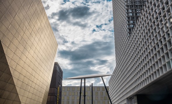 Art installation of discs on high legs between modern-looking office buildings