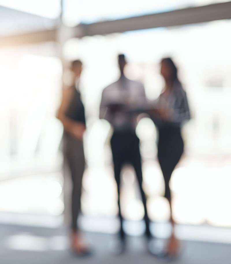 Blurred image of three professionals, one mand and two women, in office clothes standing up 